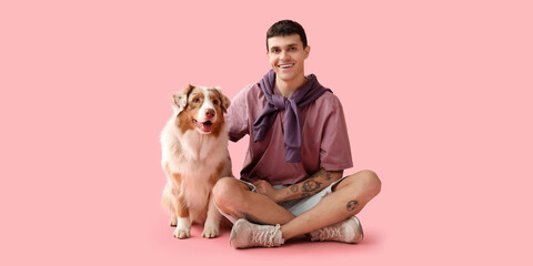 Young man with Australian Shepherd dog sitting on pink background - obrazy, fototapety, plakaty