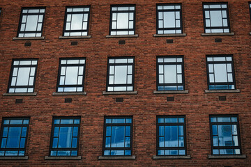 Fototapeta na wymiar Facade of a brick building with symmetrical windows reflecting the sky in Leeds, UK.
