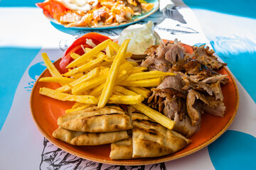 Plate with Gyros meat, pita bread, tomatoes and french fries on table in Greek restaurant, Adamas port, MIlos island, Cyclades, Greece - 767422413