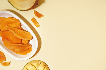 Plate with slices of dried mango on yellow background