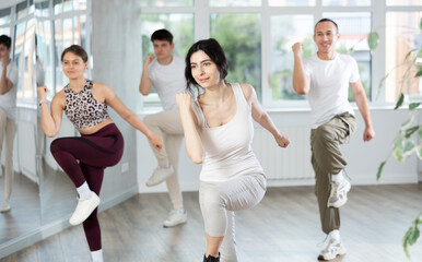 Young sports girl rehearsing modern dances during group training in light dance studio