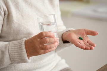 Fototapeta na wymiar Senior woman with pill and glass of water in kitchen, closeup