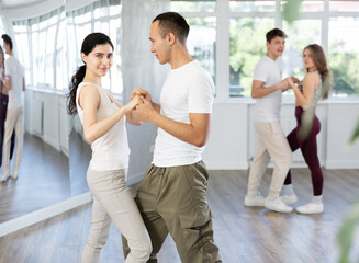 Cheerful fit young girl practicing passionate samba with interested attentive guy in dance class...
