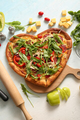 Wooden board with tasty heart shaped pizza and ingredients on light blue background