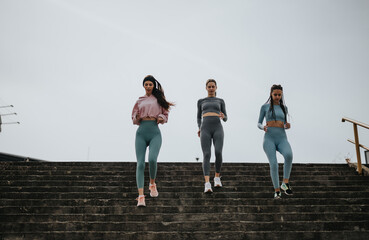 Three diverse women in sportswear descending stairs, showcasing fitness and friendship outdoors