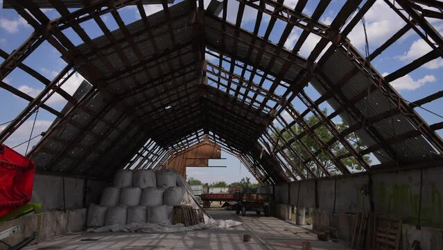 Collapsed roof of farm warehouse after shelling. Warehouse with torn roof, machinery and bags of crops inside. Concept of destruction, war, neglect