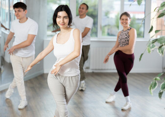 Positive young girl dancing vigorous swing with other people during group training in dance hall