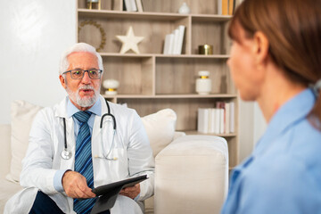Senior man doctor examining young woman in doctor office clinic or at home. Girl patient and doctor...