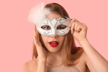 Beautiful young woman in white carnival mask on pink background