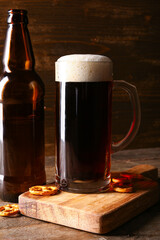 Mug and bottle of cold dark beer with pretzels on table against wooden background