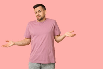 Handsome worried young man shrugging on pink background