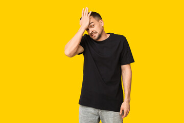 Handsome ashamed young man covering face with hand on yellow background