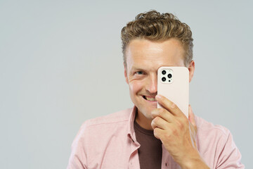 A man is holding a cell phone up to his face, looking at the camera. Concept of humor and playfulness, as the man is pretending to take a selfie with his phone