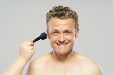 A man is smiling while brushing his hair. The man is wearing a black shirt and has a beard