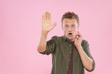 A man is on the phone and waving his hand. The man is wearing a green shirt and has a surprised expression on his face