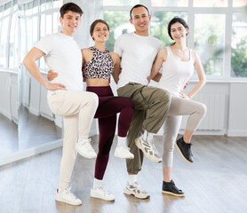 Multicultural group of enthusiastic cheerful young girls and guys traditionally lining in row while performing Greek sirtaki during dance class in sunny studio