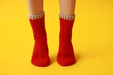 Legs of young woman in warm red knitted socks on yellow background