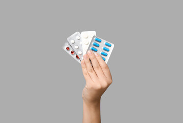 Female hand holding pills in blister packs on grey background