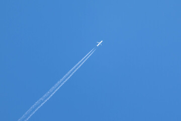 An airplane crossing the blue sky leaving a white trail of steam.