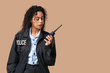 Beautiful young African-American policewoman with radio transmitter on brown background