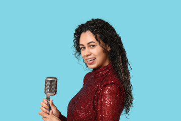 Beautiful young happy African-American female singer with microphone on blue background