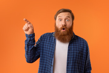 Funny portrait of surprised redhaired man with beard pointing aside