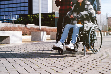 Close-up of a person in a wheelchair with friends walking alongside on city pavement.