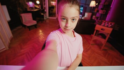 Cute kid holding selfie smartphone camera, filming herself doing room tour to children watching her online content. Young girl doing POV style video presenting her home to social media channels fans