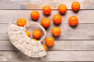 Wicker bag with sweet mandarins on grey wooden background