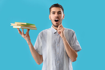 Shocked young man with books on blue background