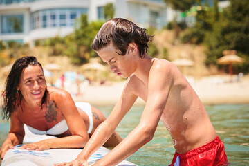 Mom with her teen son lying on a swimming board. Happy european family having fun floating on a...
