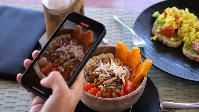 Phone in hand takes pictures of vegan dish in smoothie bowl. Slow motion video of pieces of fruit in smoothie bowl, sandwiches with tomatoes and avocado spread. Vegan food concept in smoothie bowl 