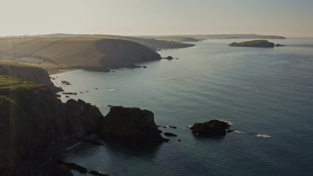 Drone aerial view of cliffs & beach coastline at Ayrmer Cove and Burgh Island, Bigbury, South Hams, Devon just after sunrise on calm, tranquil spring morning. Beautiful coastline footage