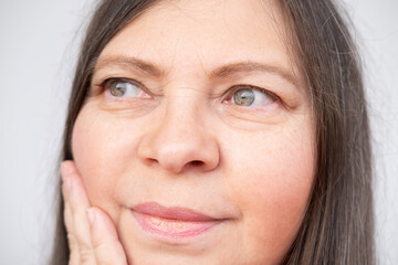 mature woman gently touches face, accepting visible signs aging such wrinkles, sagging skin and...