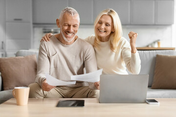 Couple excited with paperwork in front of a laptop