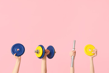 Female hands with dumbbells against pink background