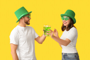 Beautiful young couple in leprechaun hats with glasses of beer on yellow background. St. Patrick's...