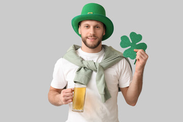 Young man in leprechaun hat with glass of beer and clover on grey background. St. Patrick's Day...