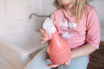 cleaning spray bottle detergent for various surfaces in kitchen in children's hands close-up,...