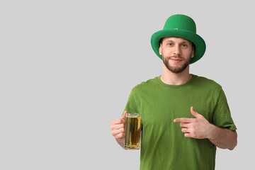 Young man in leprechaun hat with glass of beer on grey background. St. Patrick's Day celebration