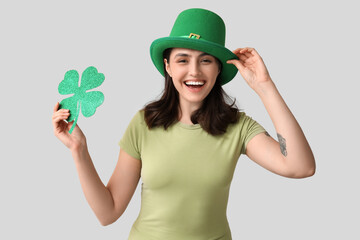 Happy young woman in leprechaun hat with clover on grey background. St. Patrick's Day celebration