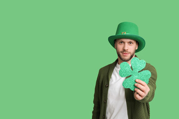 Young man in leprechaun hat with clover on green background. St. Patrick's Day celebration