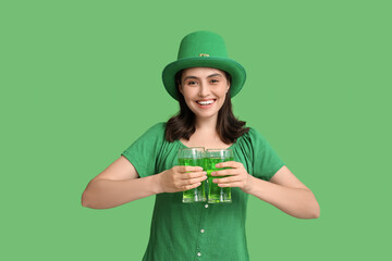 Beautiful young woman in leprechaun hat with glasses of beer on green background. St. Patrick's Day...