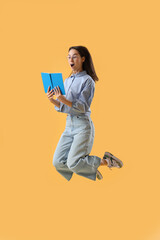 Surprised young woman with book jumping on yellow background