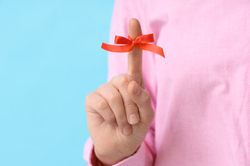 Woman with red bow on index finger against blue background. Reminder concept
