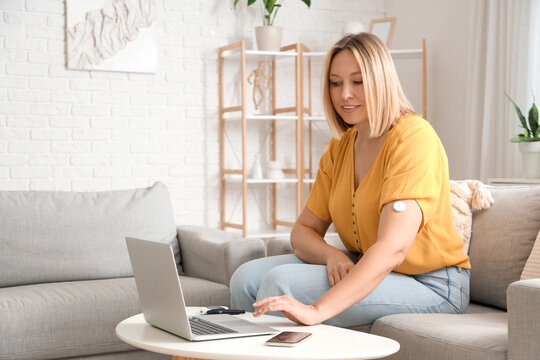 Diabetic woman with glucose sensor using laptop for measuring blood sugar level at home