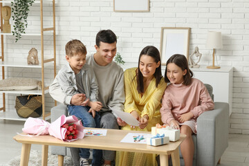 Happy couple and children with bouquet of flowers and gift at Mothers Day in living room