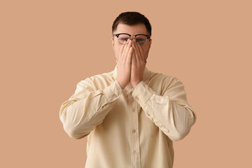 Tired young man with eyeglasses on beige background
