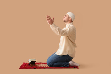 Young Muslim man with prayer mat and Koran praying on beige background