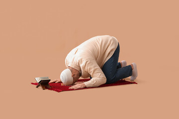 Young Muslim man with prayer mat and Koran praying on beige background